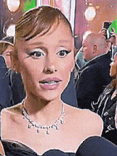 a woman wearing a necklace and a black dress is sitting in a crowd .