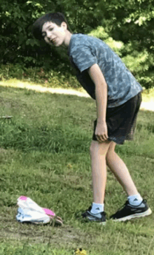 a young boy is bending over in the grass next to a pair of pink shoes .