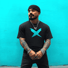 a man wearing a black shirt with a blue x on it stands in front of a blue wall