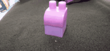 a pink lego block is sitting on top of a brown carpet .