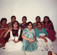 a group of women posing for a picture with one wearing a green saree