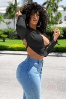 a woman with curly hair is wearing a crop top and blue jeans .