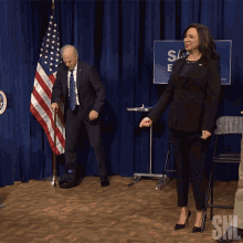 a man in a suit and tie and a woman in a black suit are dancing in front of a sign that says snl