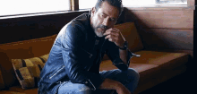 a man in a leather jacket is sitting on a couch looking down .