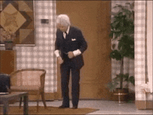 a man in a suit is standing in a living room with a chair and a plant .