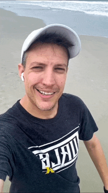 a man wearing a hat and a t-shirt that says " hurley " is smiling on the beach