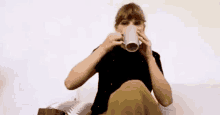 taylor swift is sitting on a couch drinking a cup of coffee .