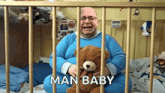a man is crying while holding a teddy bear in a crib with the words man baby written above him
