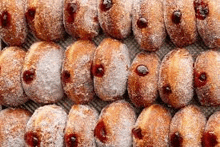 a bunch of donuts covered in powdered sugar and jam are lined up on a table .