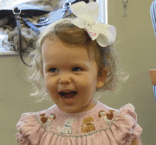 a little girl wearing a pink dress has a bow in her hair that says s on it