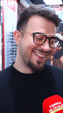 a man wearing glasses is smiling in front of a red microphone that says fabrica de culos