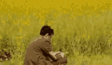 a man is sitting in a field of yellow flowers holding a cat .