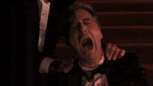 a man in a tuxedo with blood on his shirt is being held by another man