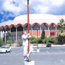 a woman stands on a pole in a parking lot in front of a building that says ' phoenix ' on it