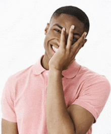 a young man in a pink polo shirt is covering his face with his hand .