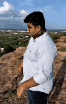 a man in a white shirt is standing on top of a rocky hill holding something in his hand .