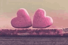 two pink hearts are sitting next to each other on a piece of wood .