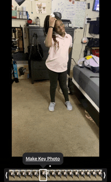 a girl in a pink shirt and black pants is standing in a bedroom with a make key photo button