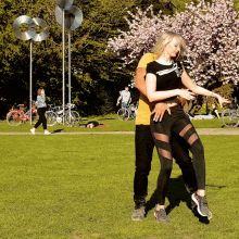 a man and woman are dancing in a park with a woman wearing a black shirt that says emporio armani