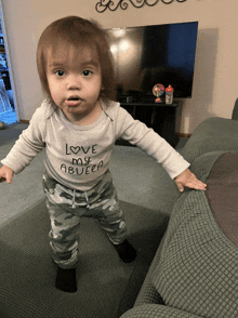 a baby wearing a shirt that says love my abuela stands on a couch