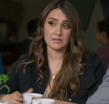 a woman in a black jacket is sitting at a table talking to someone