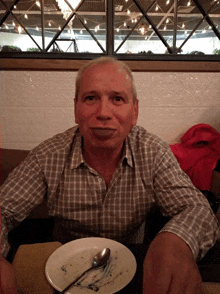 a man in a plaid shirt sits at a table with a plate of food