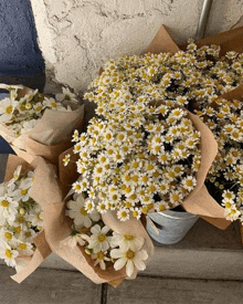 a bunch of daisies wrapped in brown paper sitting on a sidewalk