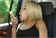 a woman is sitting in a car with her mouth open and looking at her phone .