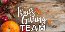 a wooden table topped with pumpkins , apples , and leaves with the words `` happy thanksgiving team '' .