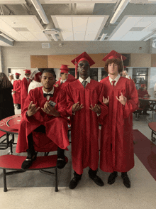 three graduates in red gowns pose for a picture in a cafeteria