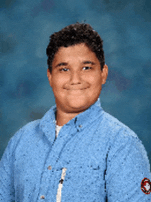 a young boy in a blue shirt smiles for the camera