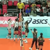 a group of women are playing volleyball on a court in front of a asics ad .