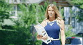 a woman in a blue dress is holding a binder while walking down the street .