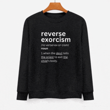 a black sweatshirt that says reverse exorcism is hanging on a wooden hanger