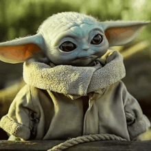 a baby yoda doll is sitting on a fence with a rope around his neck .