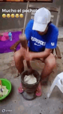 a man in a kentucky shirt is sitting in a chair using a mortar and pestle to make food .