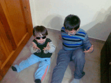 a boy wearing sunglasses sits next to a boy wearing a striped shirt