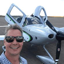 a man wearing sunglasses stands in front of a small silver airplane with the letters cirrus on the side