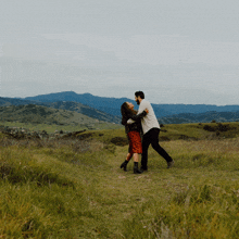 a man and a woman are dancing in a grassy field with mountains in the background