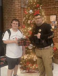 two men standing in front of a christmas tree one of whom is wearing a shirt that says crayons