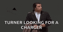 a man in a suit is looking for a charger while standing in front of a black wall .