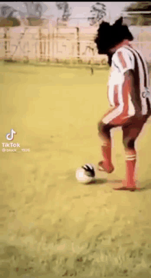 a man in a striped shirt is kicking a soccer ball .