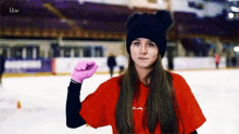 a girl wearing a red shirt and a black hat stands on an ice rink with itv written on the bottom