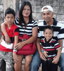 a family is posing for a picture while sitting on a bench in front of a wall .