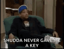 a man in a suit and hat is sitting in a chair with his legs crossed and says `` shudda never gave me a key ''