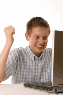 a young boy sitting in front of a laptop with his fist up