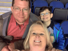 a man in a red shirt is sitting next to a woman and a boy with glasses