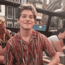 a young man wearing headphones and a striped shirt is smiling while sitting at a table with other people .