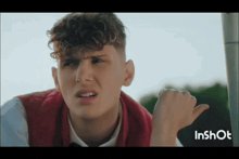 a young man with curly hair is wearing a red vest and a white shirt
