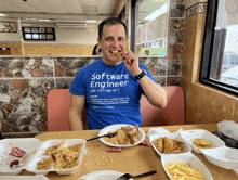 a man wearing a blue software engineer t-shirt is eating food